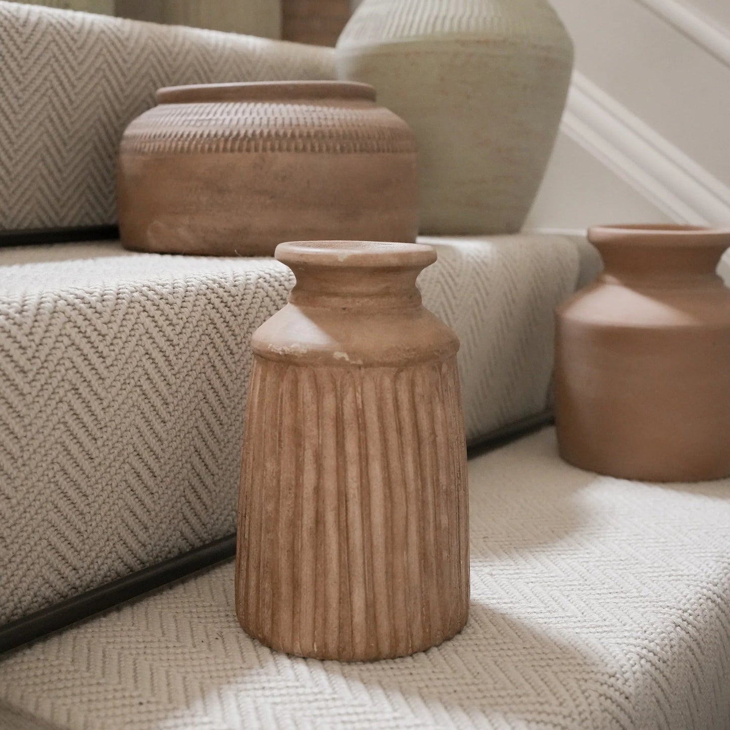 Decorative terracotta vases and containers on a textured surface with a neutral background