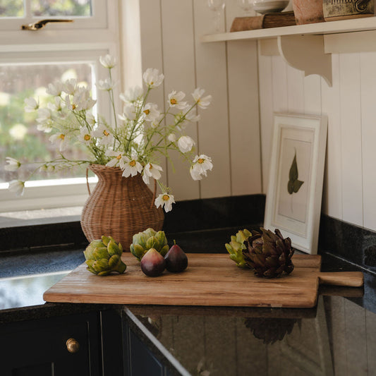 Kitchen counter with a cutting board, flowers, and a plant on a shelf.