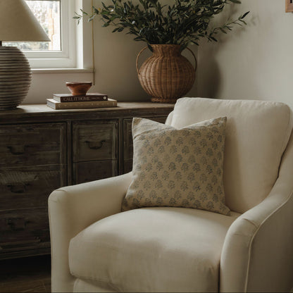 Cozy living room with a white armchair, decorative pillow, and a vase with greenery on a wooden side table.