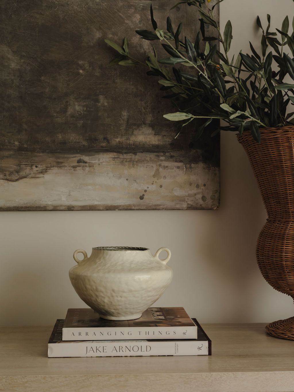 Decorative vase on books with a plant and painting in the background