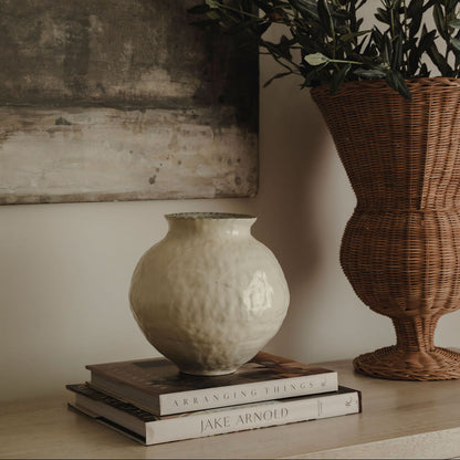 Decorative setup with a white vase, wicker basket, and books on a surface.