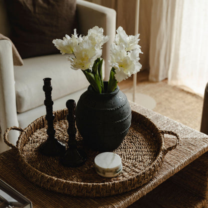Decorative vase with white flowers on a woven tray in a living room setting
